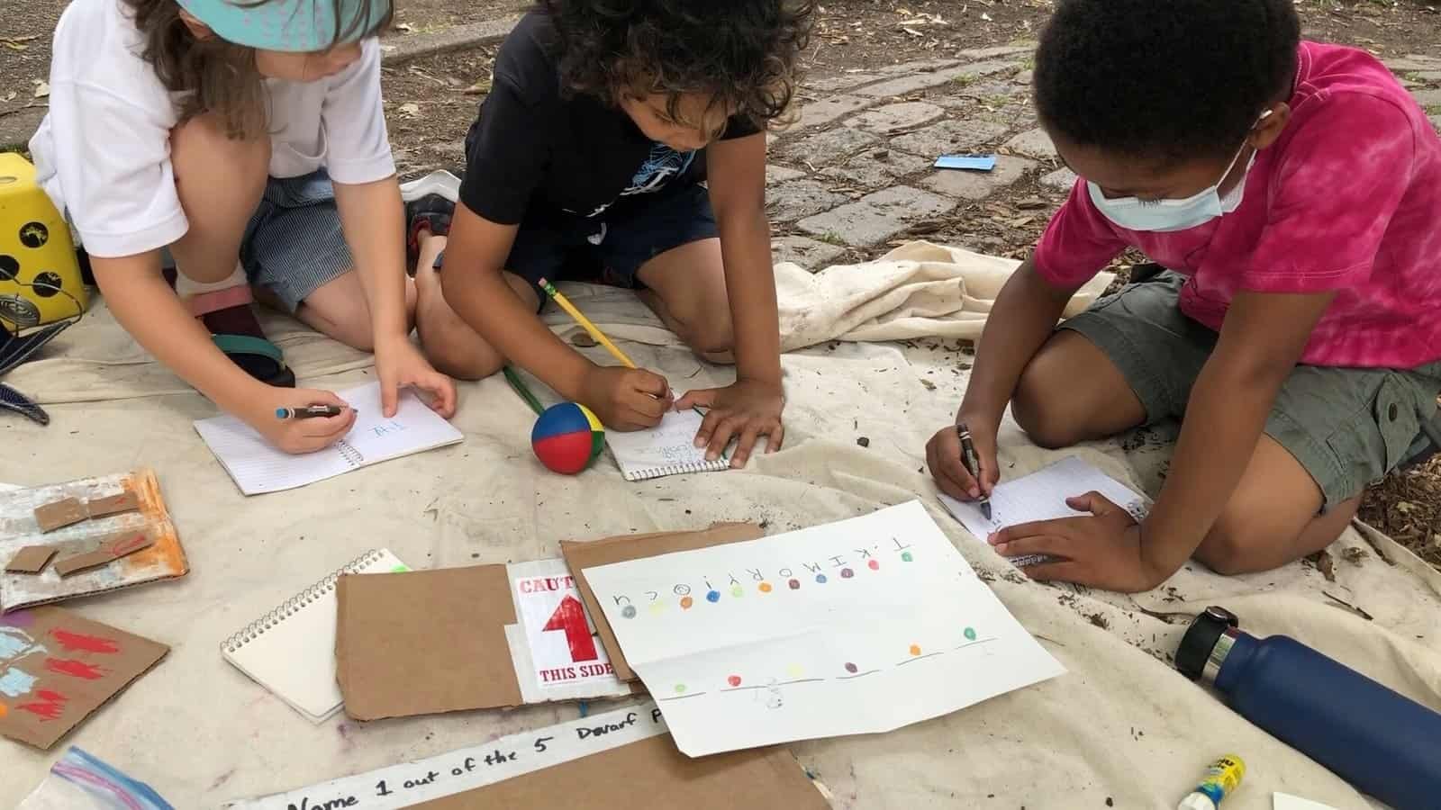 a group of children sitting on a blanket writing on notebooks